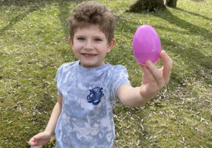 chłopiec pokazuje znalezione w ogrodzie kolorowe jajko
